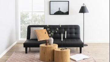 Rustykalny salon z czarną pikowaną kanapą i stolikami z tworzywa sztucznego